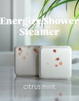Two shower steamers labeled 'Energize Shower Steamer' with 'citrus mint' scent on a reflective surface.