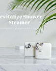 Two marble-patterned shower steamers on a marble countertop with a plant in the background.