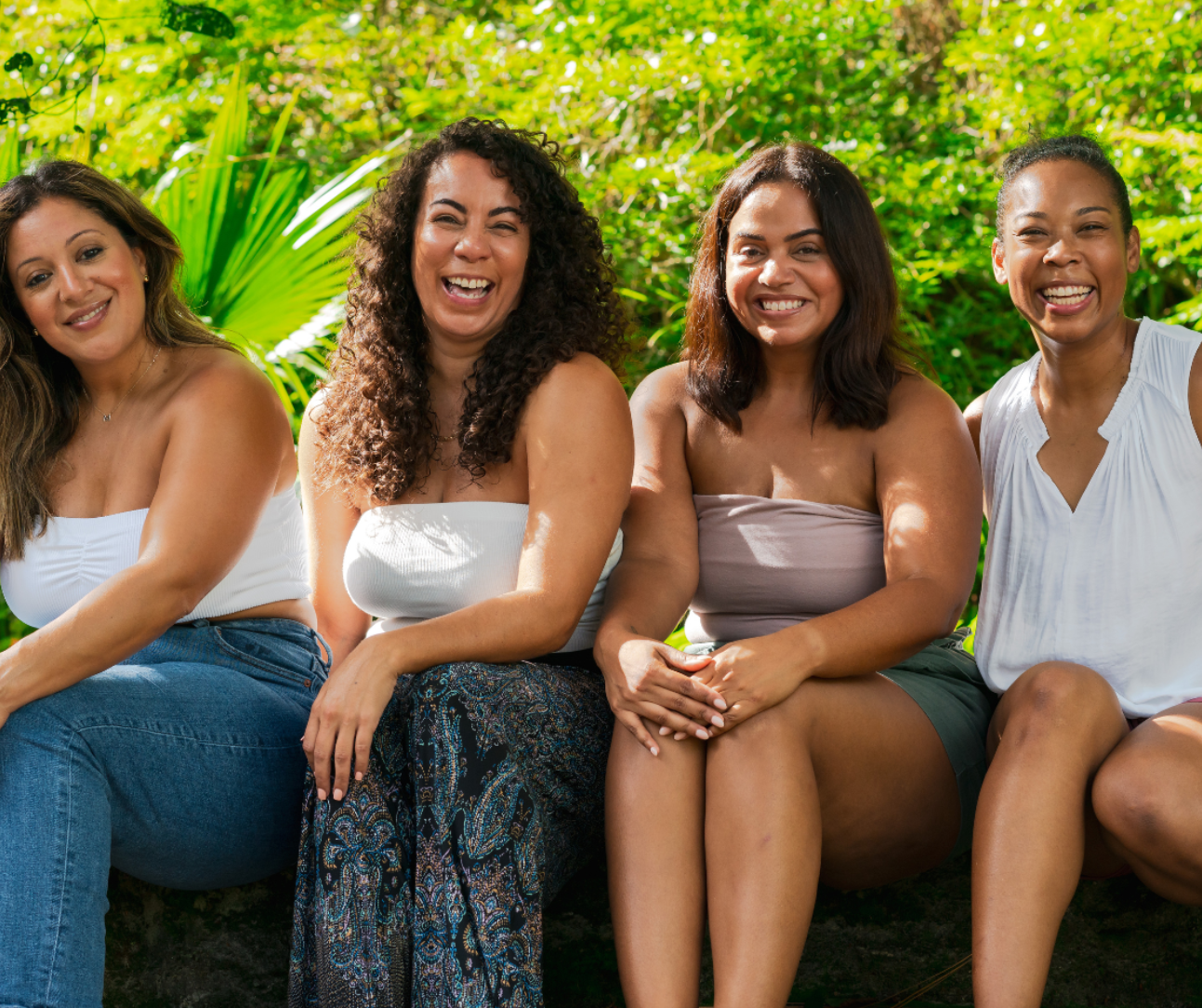 Four women sitting together outdoors with greenery in the background