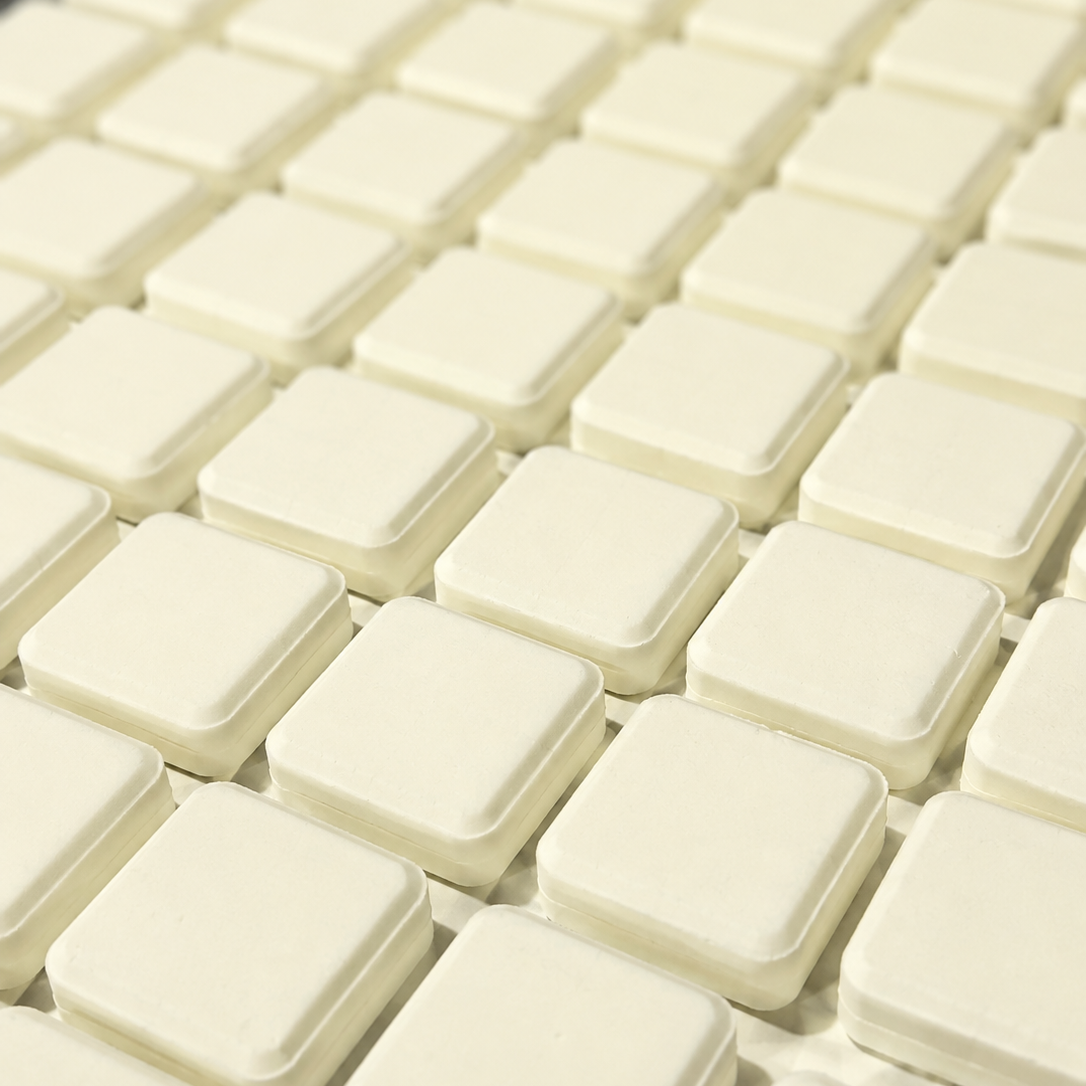 A close-up view of multiple small square off-white plastic or rubber pads arranged in rows on a tray or surface.