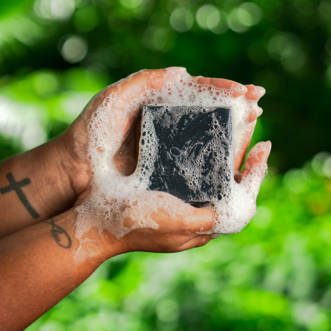 Detox black soap bar held in hands with a fluffy lather of soap suds surrounding soap bar