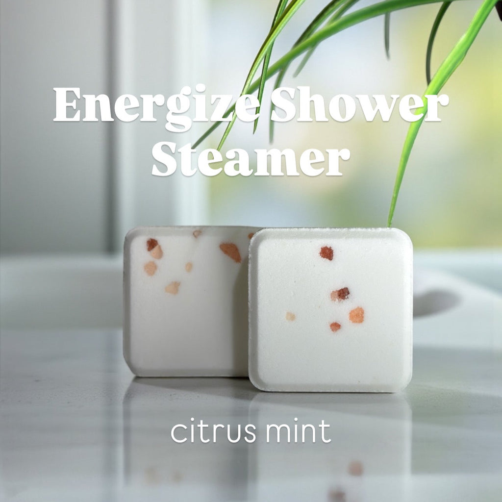 Two shower steamers labeled 'Energize Shower Steamer' with 'citrus mint' scent on a reflective surface.