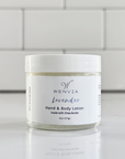 A jar of WENVIA Hand & Body Lotion with a label that reads 'Lavender' and 'made with Shea Butter'. The jar is placed against a tiled wall.