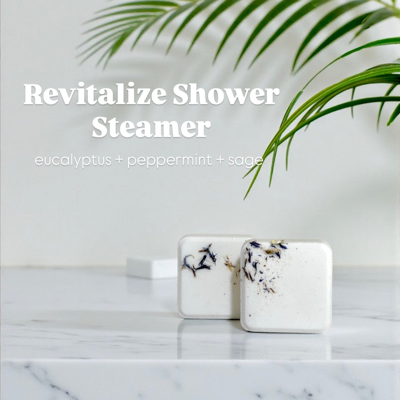 Two marble-patterned shower steamers on a marble countertop with a plant in the background.