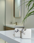 Two decorative shower steamers on a white surface with a blurred bathroom background