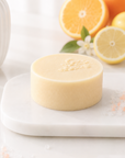 Bar of soap on a white surface with oranges and lemons in the background